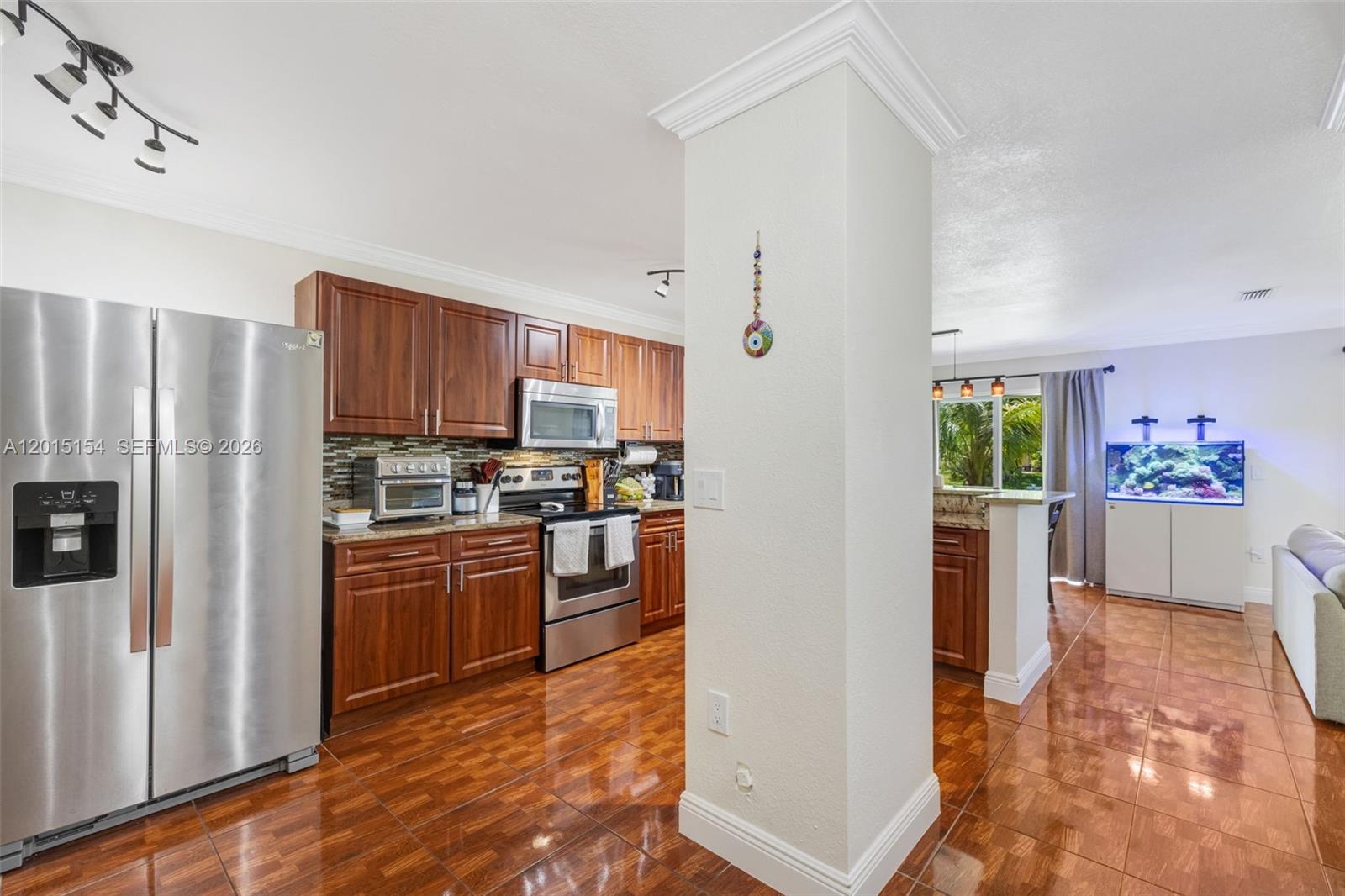 A kitchen with wood cabinets and stainless steel appliances opens into a living area — 9288 NW 55th St, Sunrise FL 33351, SUNRISE, FL