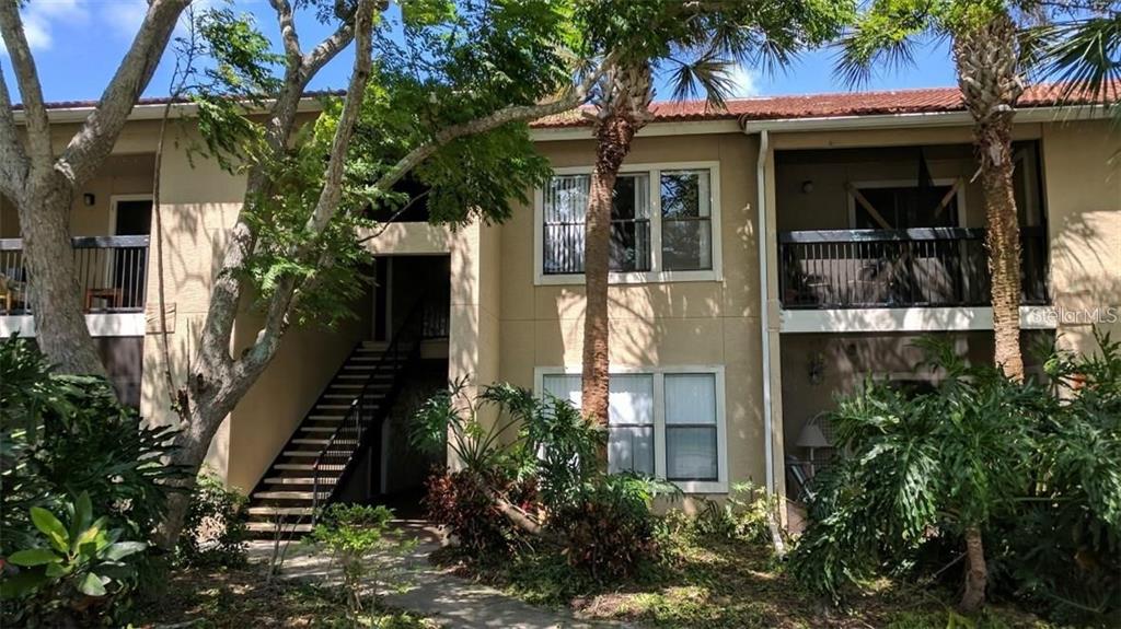 A two-story apartment building exterior with a staircase, balconies, and surrounding tropical landscaping — 4028 CROCKERS LAKE BOULEVARD UNIT 11, SARASOTA, FL