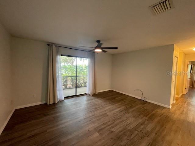 An empty room features wood-look flooring, a ceiling fan, and a sliding glass door — 4028 CROCKERS LAKE BOULEVARD UNIT 11, SARASOTA, FL