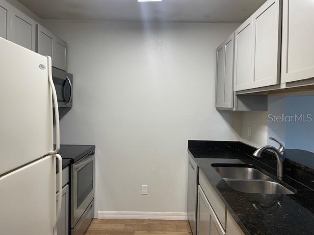 A kitchen features light gray cabinets, black countertops, stainless steel appliances, and a white refrigerator — 4028 CROCKERS LAKE BOULEVARD UNIT 11, SARASOTA, FL