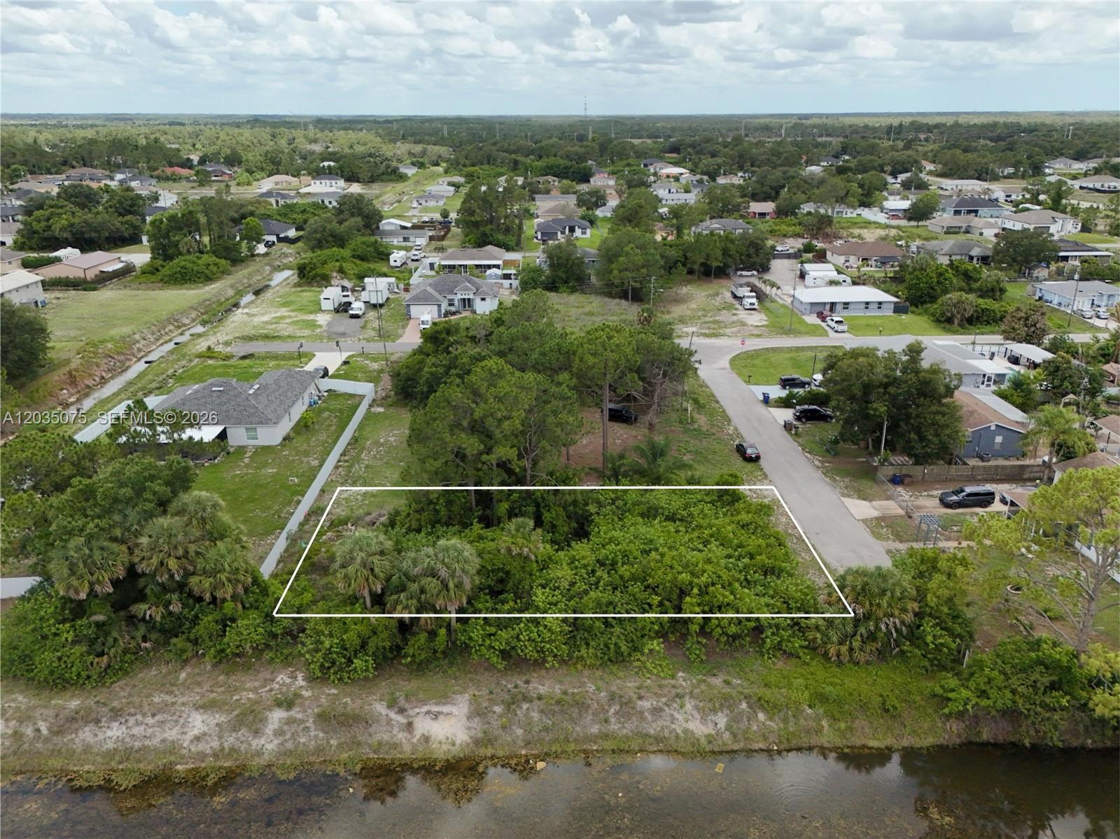 An aerial view shows a rectangular, tree-covered vacant lot bordered by a road and canal — 3105 BRIAN AVE S, Lehigh Acres FL 33976, LEHIGH ACRES, FL