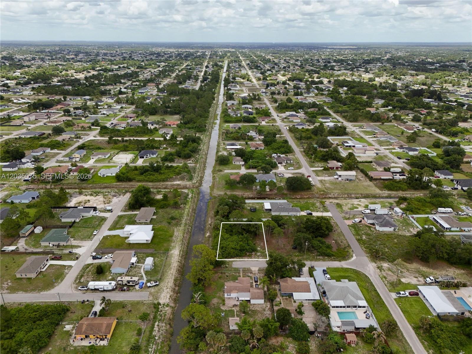 An aerial view shows a vacant, rectangular lot outlined in white next to a canal — 3105 BRIAN AVE S, Lehigh Acres FL 33976, LEHIGH ACRES, FL