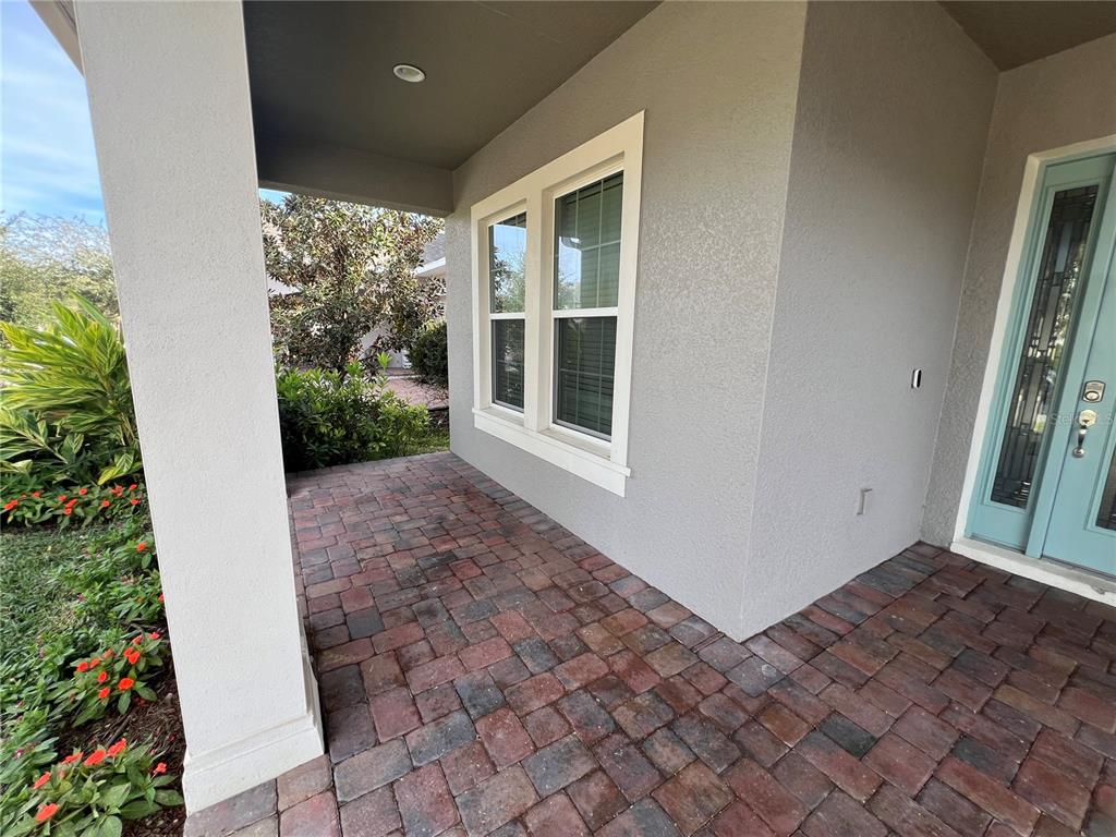 A covered front porch features brick pavers, a light gray exterior wall, and a teal door — 15784 SWEET LIMETTA DRIVE, WINTER GARDEN, FL