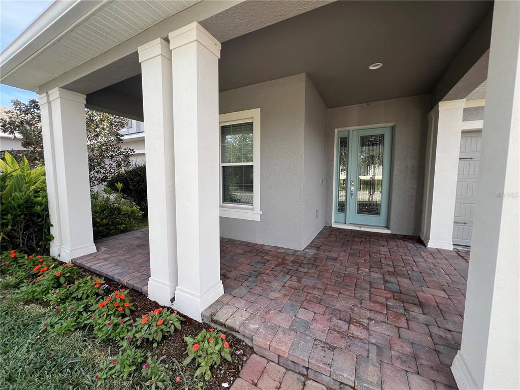 A covered front porch with paver flooring, white columns, and a light blue front door — 15784 SWEET LIMETTA DRIVE, WINTER GARDEN, FL