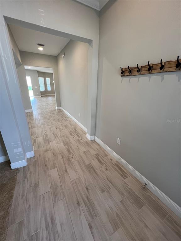 A hallway with light wood-look tile flooring and a wall-mounted coat rack — 15784 SWEET LIMETTA DRIVE, WINTER GARDEN, FL