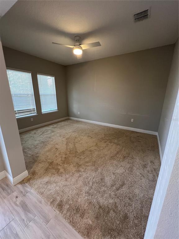 An empty bedroom features beige carpet, tan walls, two windows with blinds, and a ceiling fan — 15784 SWEET LIMETTA DRIVE, WINTER GARDEN, FL