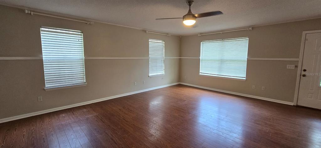 An empty living room features wood-look flooring, beige walls with chair rail molding, and windows — 5401 NW 63RD PLACE, OCALA, FL
