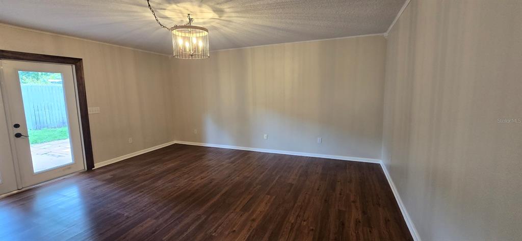 An empty room features dark wood-look flooring, light-colored walls, and a modern drum chandelier — 5401 NW 63RD PLACE, OCALA, FL