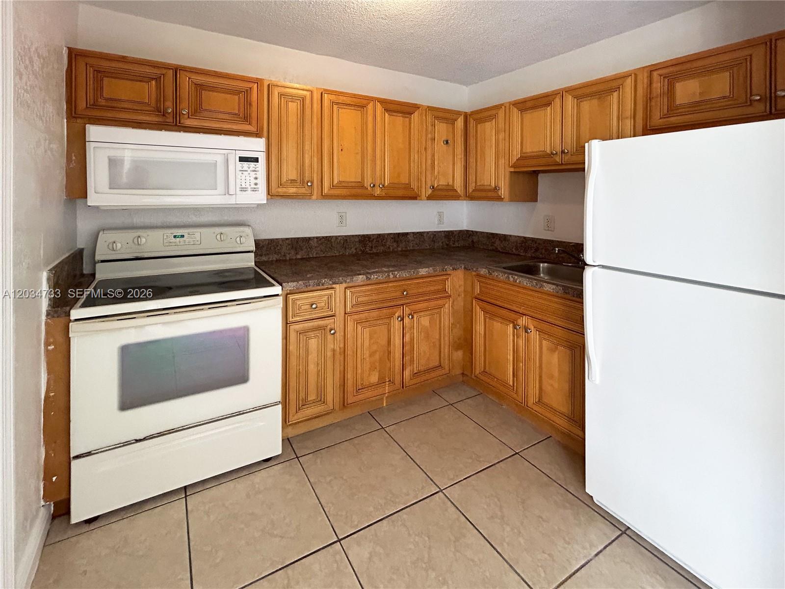 A kitchen features wooden cabinets, white appliances, brown countertops, and light-colored tile flooring — 8287 NE Miami Ct # 102, Miami FL 33138, MIAMI, FL