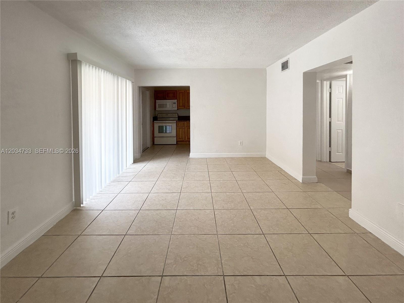 An empty room with beige tile flooring leads to a kitchen with wooden cabinets — 8287 NE Miami Ct # 102, Miami FL 33138, MIAMI, FL