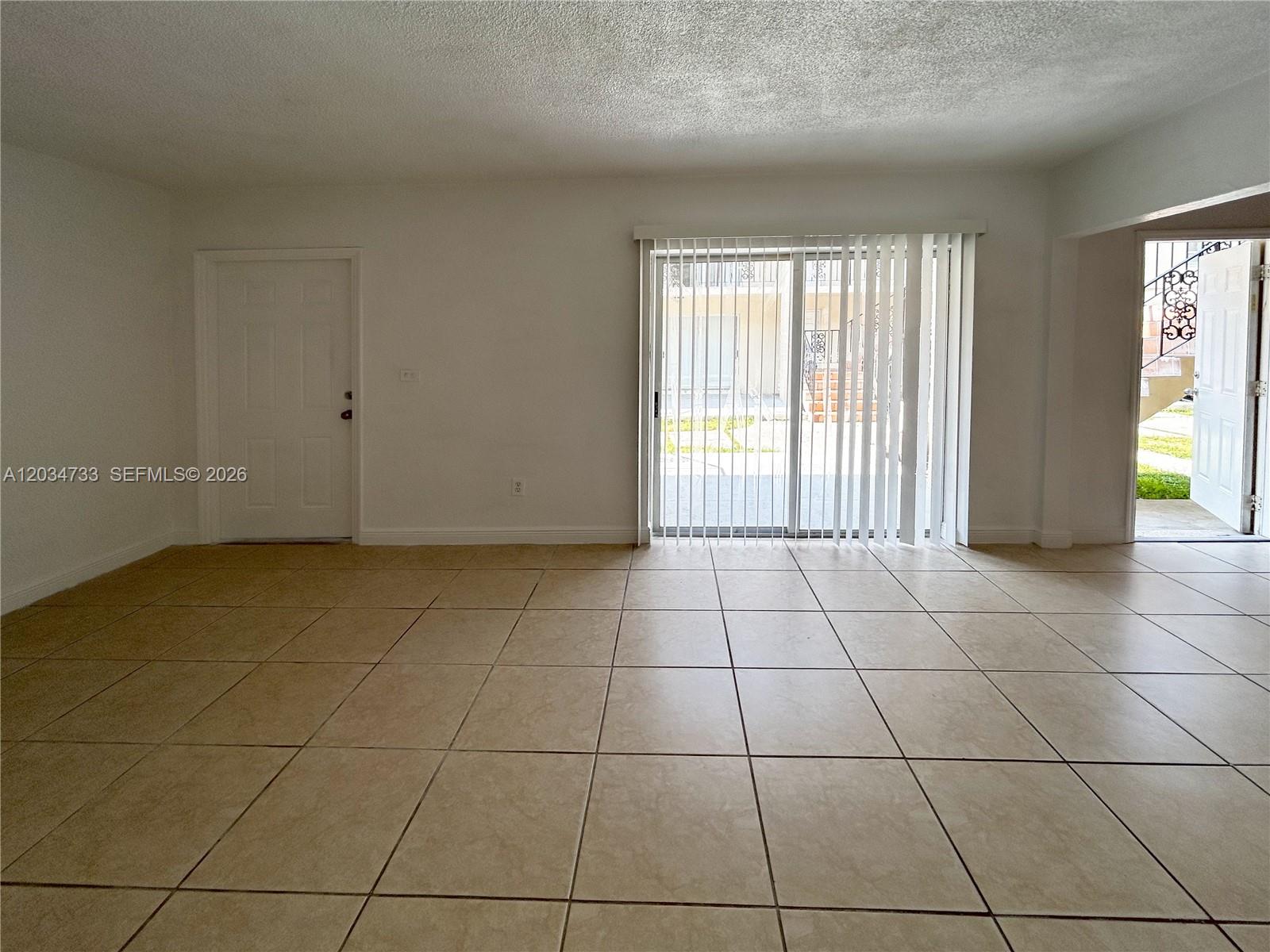 An empty room features beige tile flooring, white walls, a sliding glass door, and two doors — 8287 NE Miami Ct # 102, Miami FL 33138, MIAMI, FL