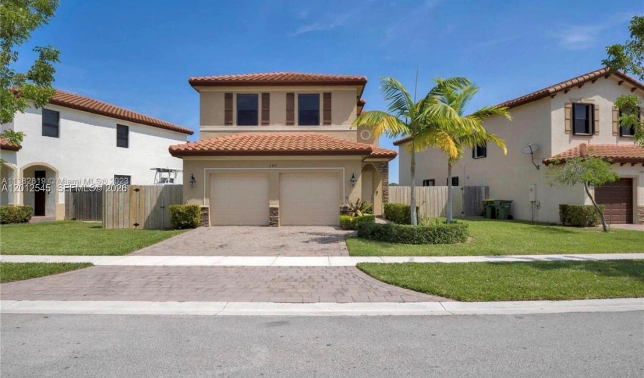 A two-story suburban house features a tan stucco exterior, a tiled roof, and a two-car garage — 2401 NE 2nd Dr, Homestead FL 33033, HOMESTEAD, FL