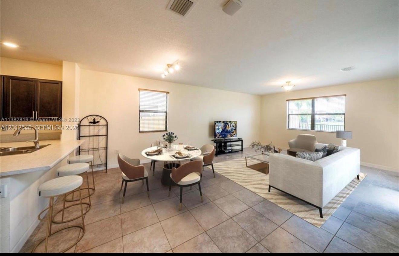 An open-concept living and dining area features tile flooring, a kitchen island, and neutral walls — 2401 NE 2nd Dr, Homestead FL 33033, HOMESTEAD, FL