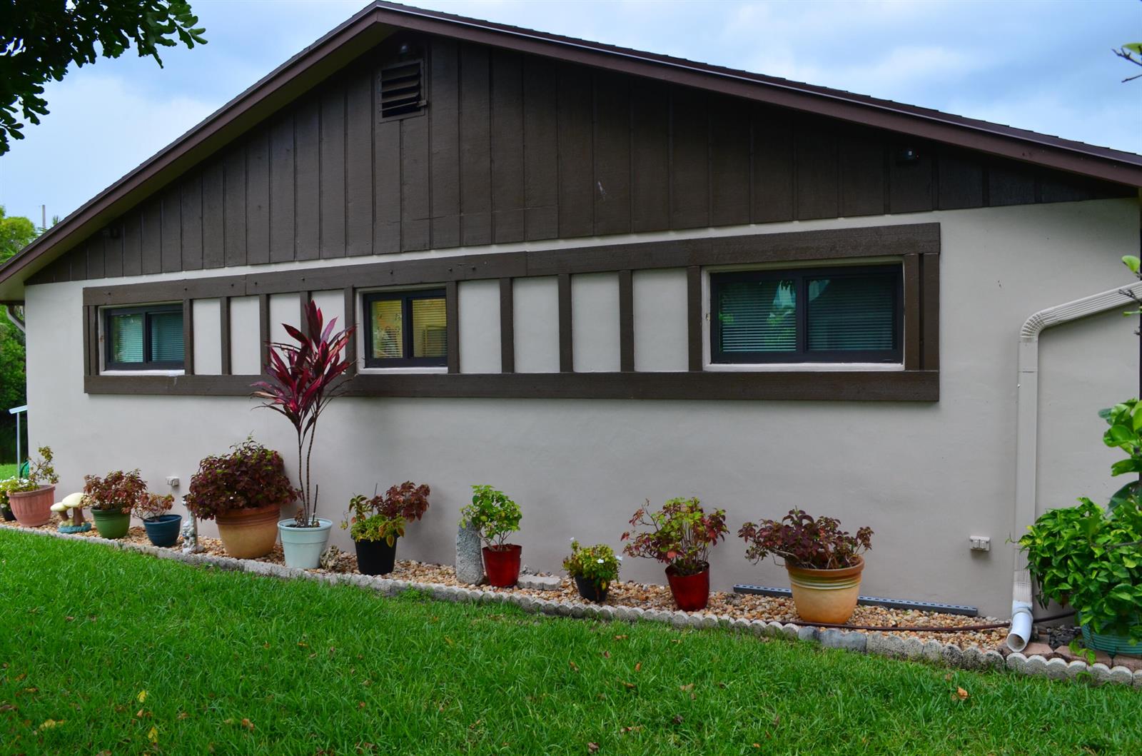 The exterior of a house features beige stucco walls, dark brown trim, and potted plants — 5392 Viburnum Circle, Delray Beach FL 33484, DELRAY BEACH, FL