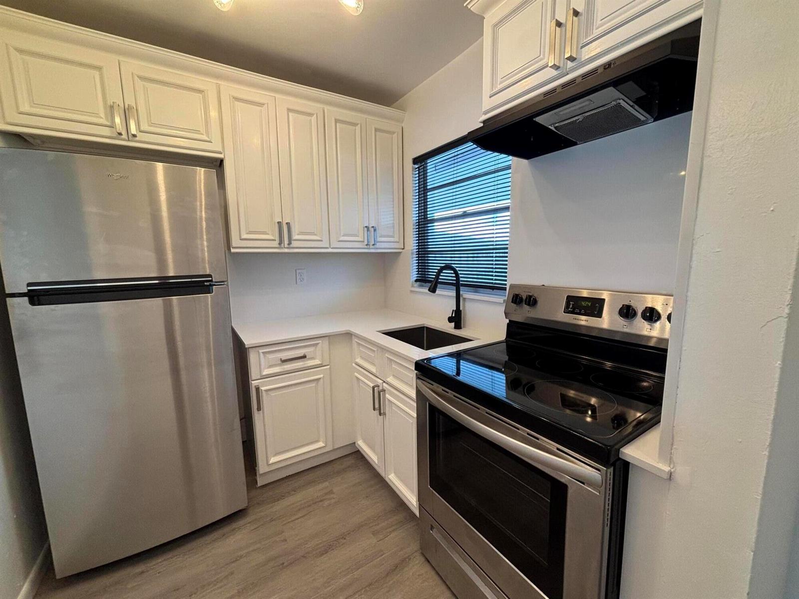 A kitchen features white cabinets, stainless steel appliances, a black faucet, and light wood flooring — 1112 Lake Terrace # 207, Boynton Beach FL 33426, BOYNTON BEACH, FL