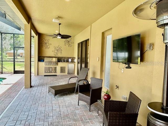 A covered outdoor patio features a built-in grill, wicker furniture, and a wall-mounted television — 22444 OAKVILLE DRIVE, LAND O LAKES, FL