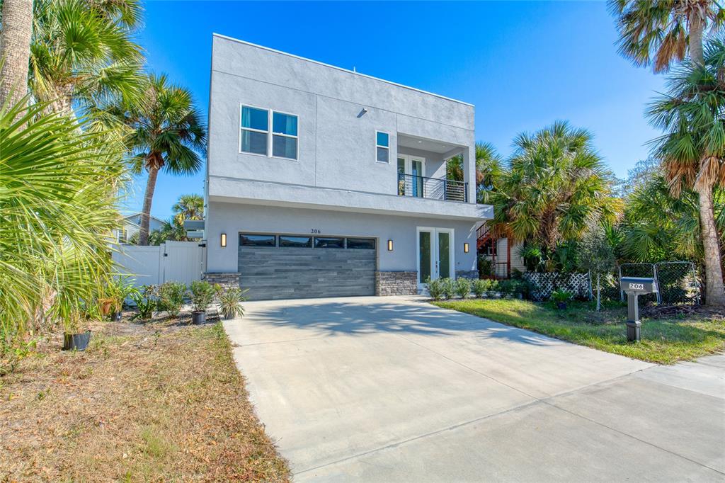A modern two-story house with a gray stucco exterior, a wood-paneled garage, and palm trees — 206 N HALIFAX AVENUE, DAYTONA BEACH, FL