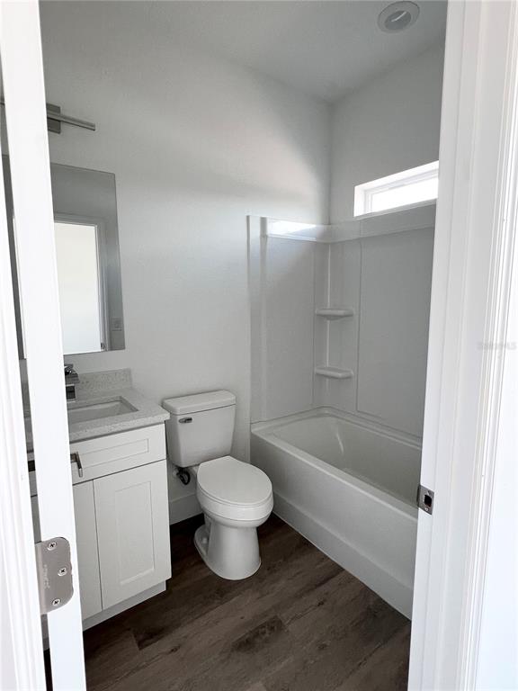 A bathroom features a white vanity, a toilet, and a tub-shower combination with wood-look flooring — 1782 CORIANDER DRIVE, POINCIANA, FL