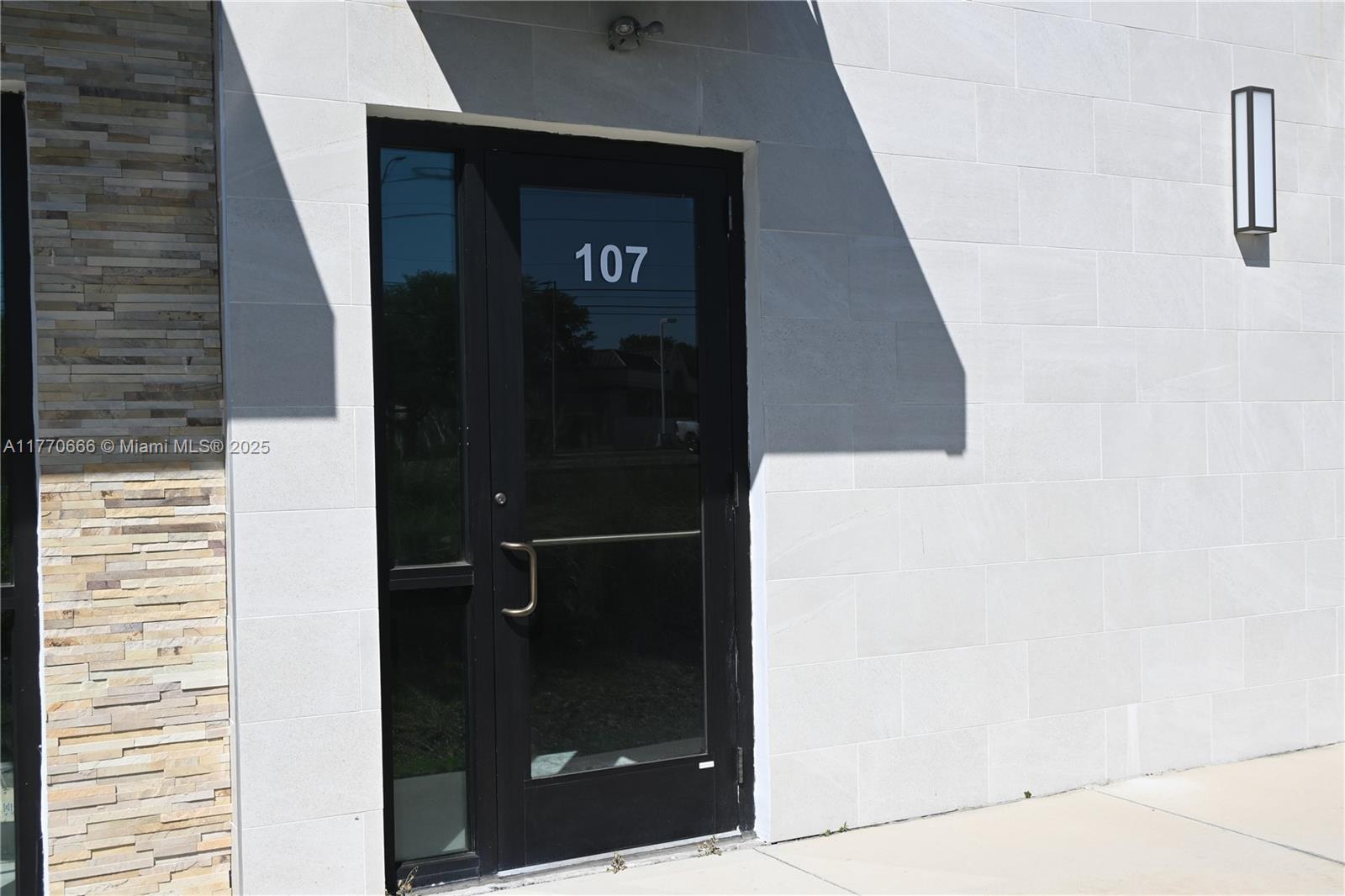 A black glass door labeled 107 is set into a white stone-tiled exterior wall — 3370 ROUSE RD # 107, Orlando FL 32819, ORLANDO, FL