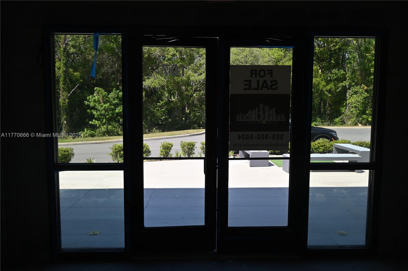 A view looking out through glass double doors at a paved parking area and trees — 3370 ROUSE RD # 107, Orlando FL 32819, ORLANDO, FL