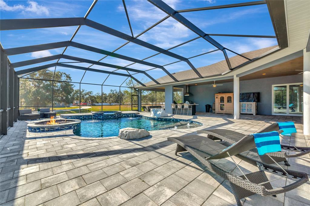 A screened-in patio featuring a swimming pool, hot tub, fire pit, and outdoor kitchen area — 28154 GOPHER HILL ROAD, MYAKKA CITY, FL