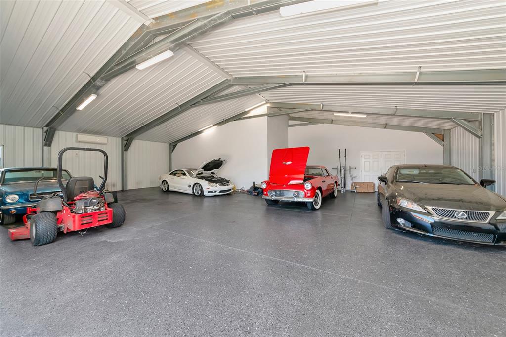 A large, open-concept garage features a concrete floor, metal ceiling, and several parked vehicles — 28154 GOPHER HILL ROAD, MYAKKA CITY, FL