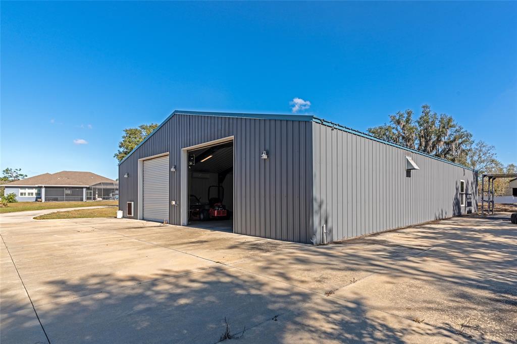 A gray metal workshop building stands on a large concrete driveway under a blue sky — 28154 GOPHER HILL ROAD, MYAKKA CITY, FL