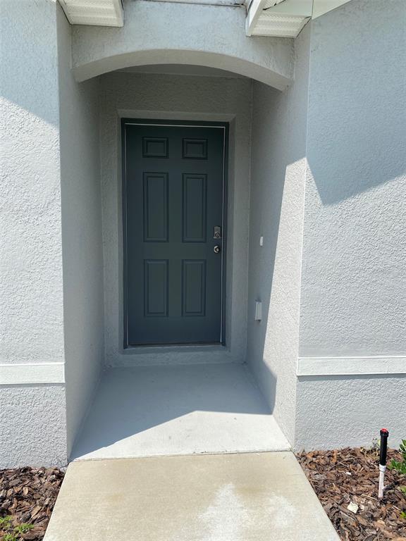 A gray front door is set within a recessed entryway of a stucco home — 4961 SW 88TH PLACE, OCALA, FL