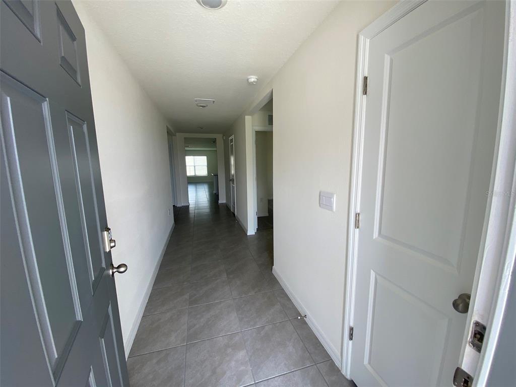 A hallway with gray tile flooring leads toward a bright room with a window — 4961 SW 88TH PLACE, OCALA, FL
