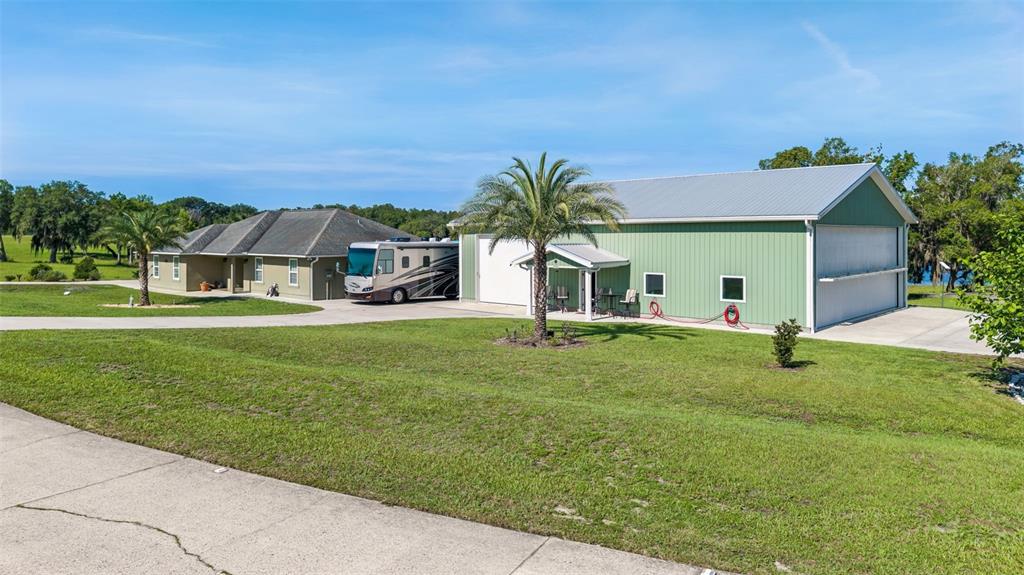 A green metal building and a tan house sit on a grassy lot with palm trees — 107 EAGLES NEST LANE, CRESCENT CITY, FL