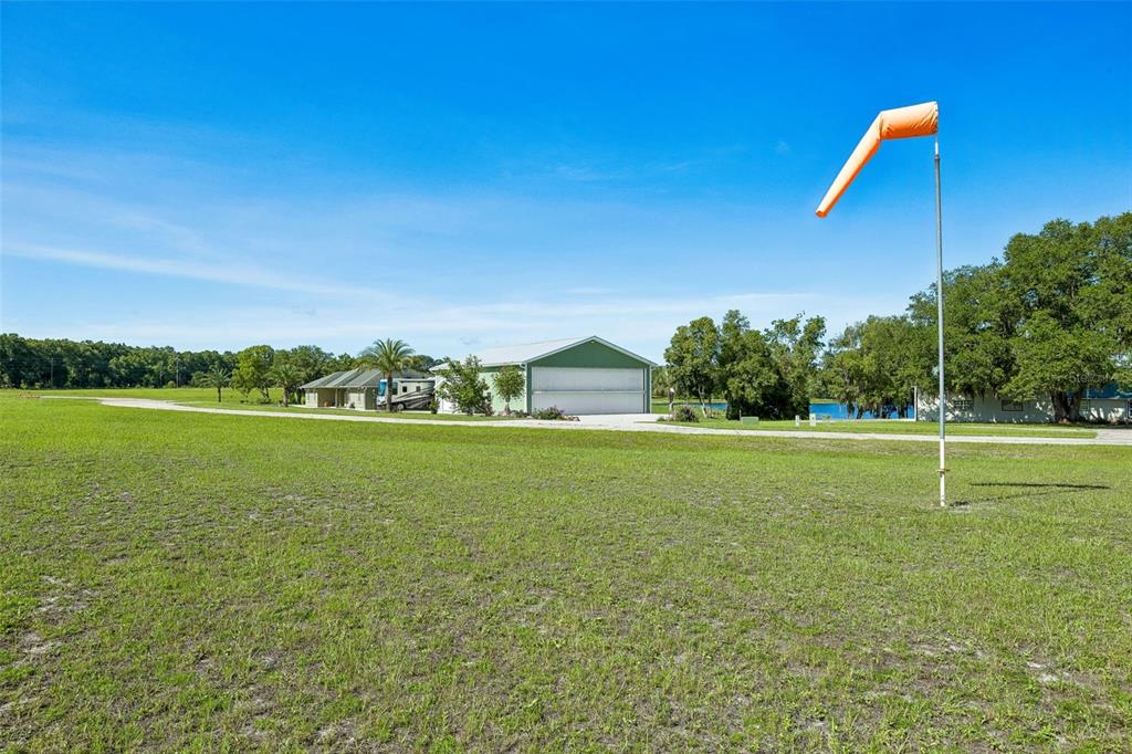 A grassy field features a windsock on a pole, a hangar, and a nearby house — 107 EAGLES NEST LANE, CRESCENT CITY, FL