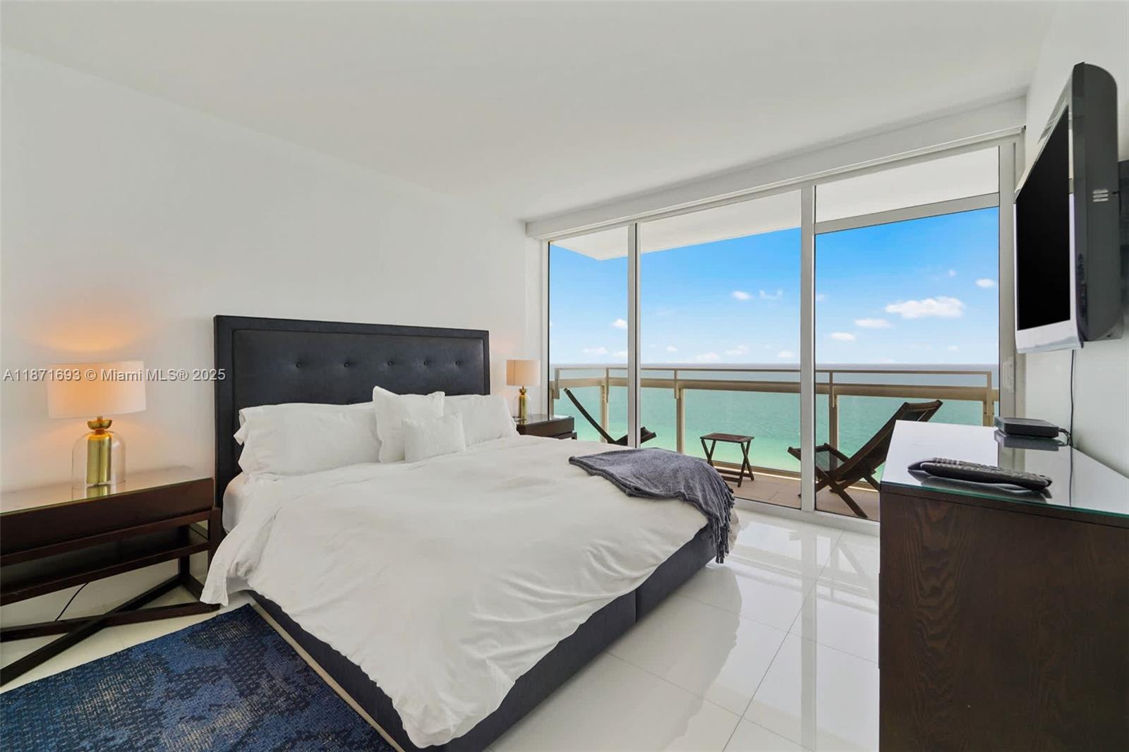 A bedroom features a king bed, white tile floors, and a balcony overlooking the ocean — 6801 Collins Ave, Miami Beach FL 33141, MIAMI BEACH, FL