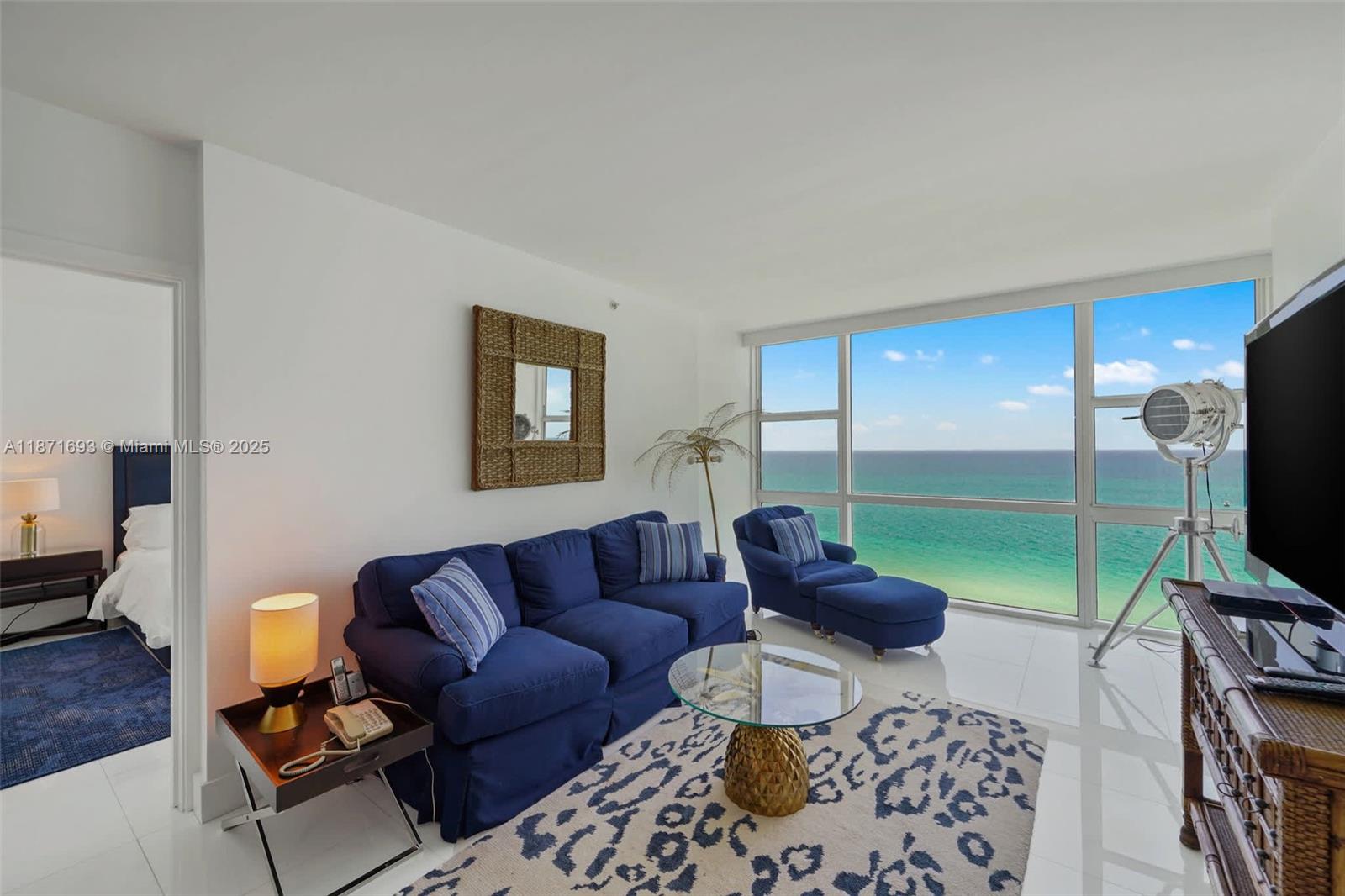 A living room features a blue sofa, a glass coffee table, and ocean views — 6801 Collins Ave, Miami Beach FL 33141, MIAMI BEACH, FL