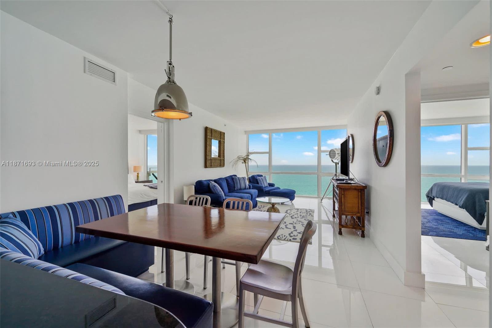 An open-concept living and dining area features white tile floors, blue furniture, and ocean views — 6801 Collins Ave, Miami Beach FL 33141, MIAMI BEACH, FL