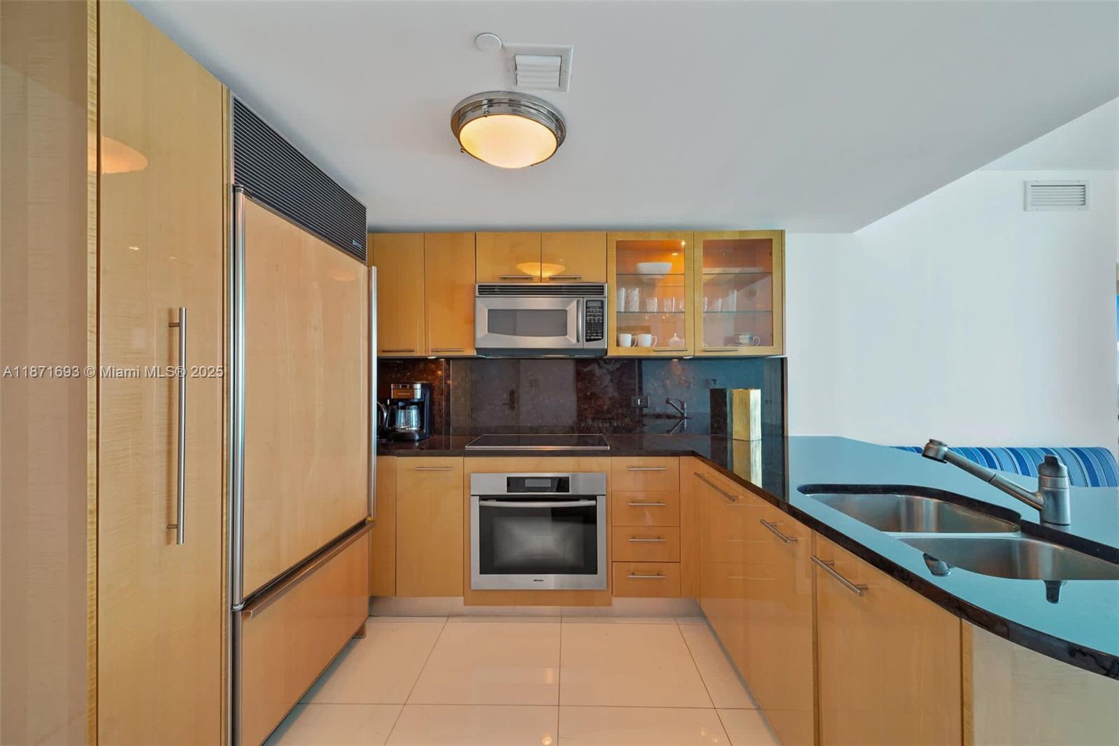 A kitchen features light wood cabinets, black countertops, stainless steel appliances, and white tile flooring — 6801 Collins Ave, Miami Beach FL 33141, MIAMI BEACH, FL