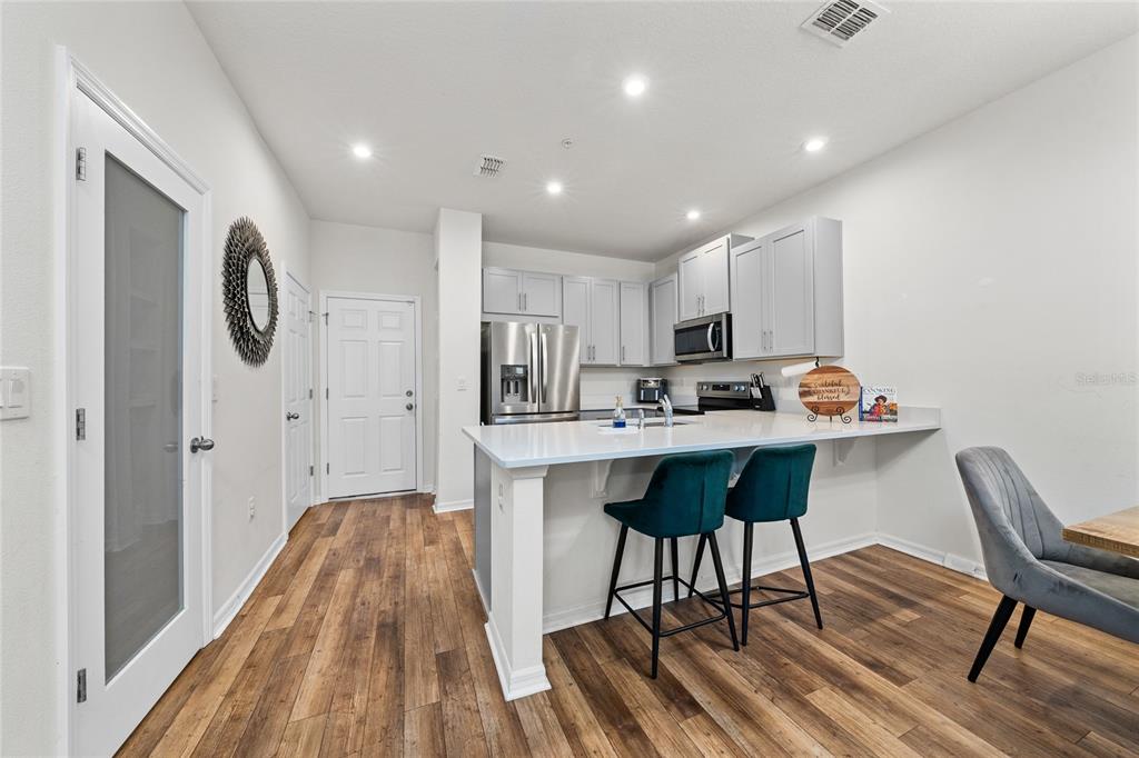A modern kitchen features light gray cabinets, a white island with two stools, and wood-look flooring — 10239 HIGHLINE CREST STREET, ORLANDO, FL