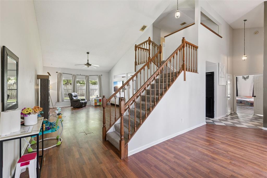 A living room with wood-look flooring, a carpeted staircase, and a vaulted ceiling — 1513 OBERLIN TERRACE, LAKE MARY, FL