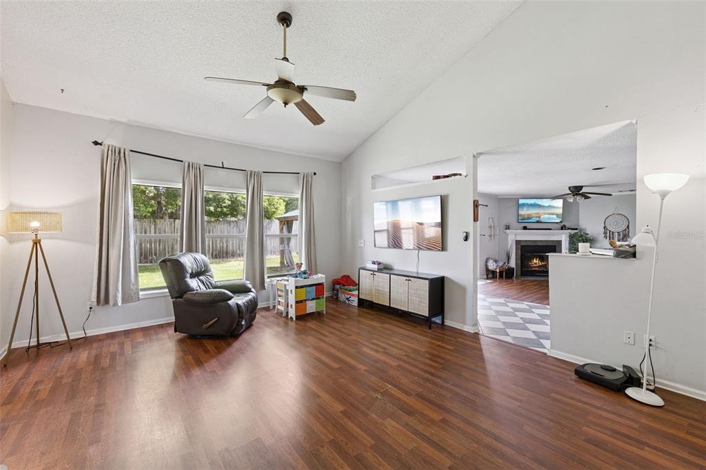 A living room features wood-look flooring, a ceiling fan, a wall-mounted television, and large windows — 1513 OBERLIN TERRACE, LAKE MARY, FL