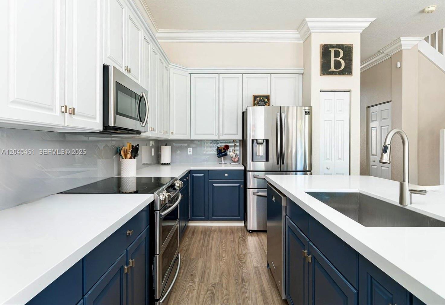 A kitchen features white upper cabinets, navy lower cabinets, stainless steel appliances, and white countertops — 208 SE 15th St, Dania Beach FL 33004, DANIA BEACH, FL
