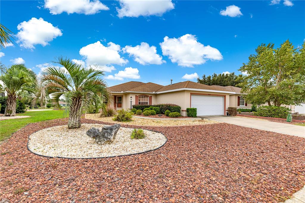 A single-story house with a tan exterior, a two-car garage, and a rock-covered front yard — 9119 SW 99TH COURT ROAD, OCALA, FL