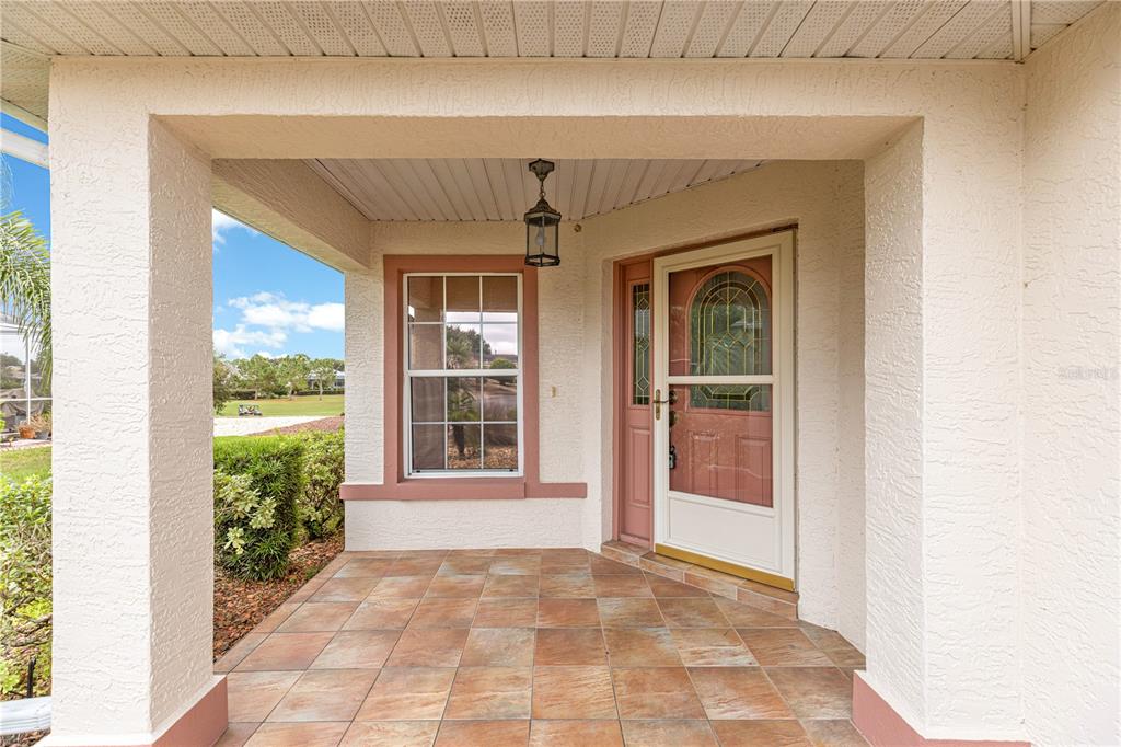 A covered front porch features tiled flooring, a single window, and a glass-paneled entry door — 9119 SW 99TH COURT ROAD, OCALA, FL