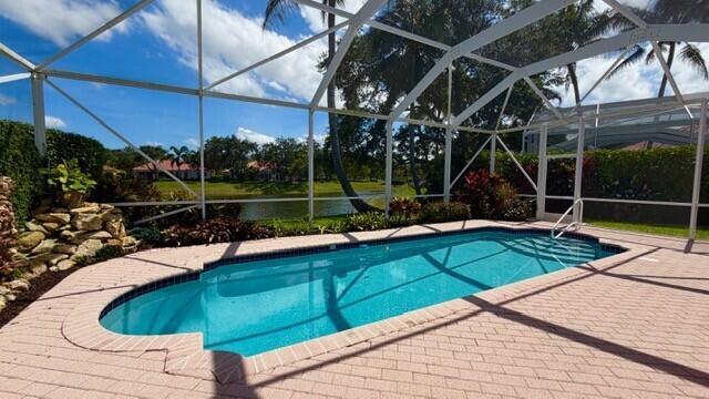A screened-in swimming pool with a stone water feature sits on a brick paver patio — 7240 Deer Point Lane, West Palm Beach FL 33411, WEST PALM BEACH, FL