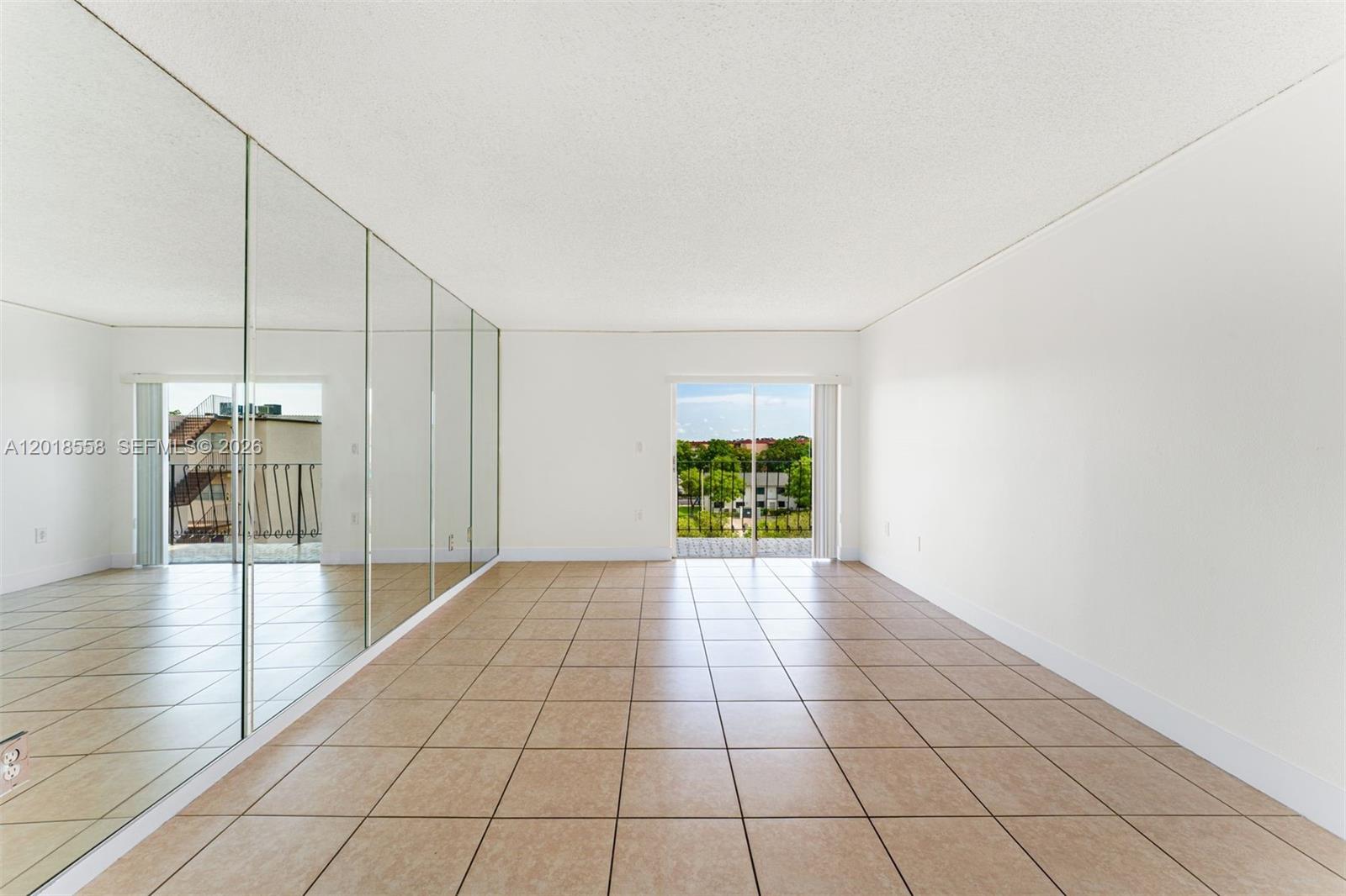 An empty room features beige tile flooring, a mirrored wall, and a sliding glass door — 1950 W 54th St # 412, Hialeah FL 33012, HIALEAH, FL