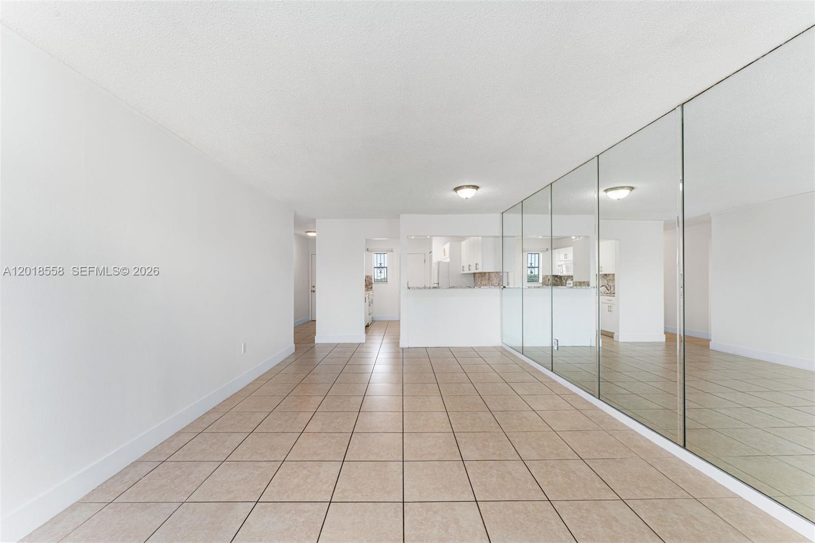 An empty room features beige tile flooring, white walls, and a large mirrored wall — 1950 W 54th St # 412, Hialeah FL 33012, HIALEAH, FL