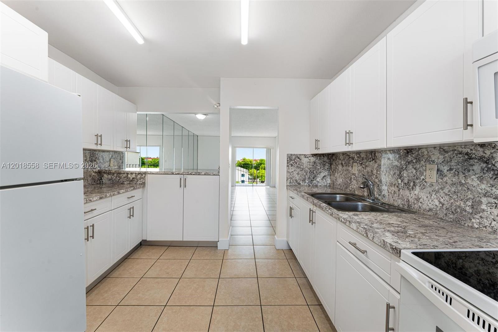 A kitchen features white cabinets, granite countertops, tile flooring, and a view of a balcony — 1950 W 54th St # 412, Hialeah FL 33012, HIALEAH, FL