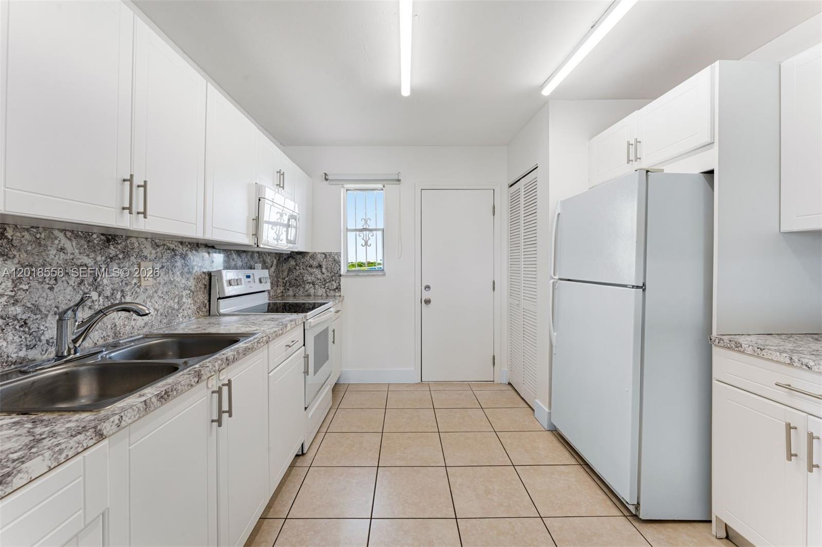 A kitchen features white cabinets, granite countertops, tile flooring, and a white refrigerator — 1950 W 54th St # 412, Hialeah FL 33012, HIALEAH, FL