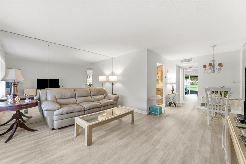 A living room with light wood-look flooring, a beige sofa, and a large mirrored wall — 24862 US HIGHWAY 19 N UNIT 806, CLEARWATER, FL