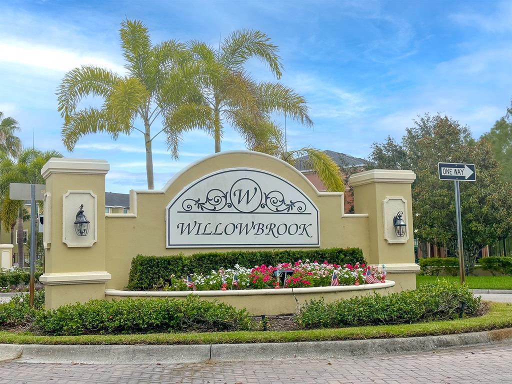 A beige stucco monument sign for Willowbrook stands in front of palm trees and landscaping — 8860 WHITE SAGE LOOP, BRADENTON, FL