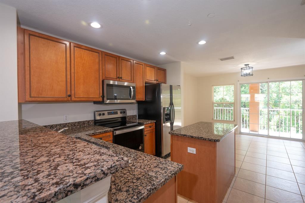 A kitchen features wood cabinets, granite countertops, stainless steel appliances, and a center island — 8860 WHITE SAGE LOOP, BRADENTON, FL