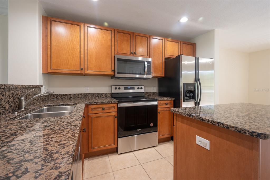 A kitchen features wood cabinets, granite countertops, stainless steel appliances, and a central island — 8860 WHITE SAGE LOOP, BRADENTON, FL